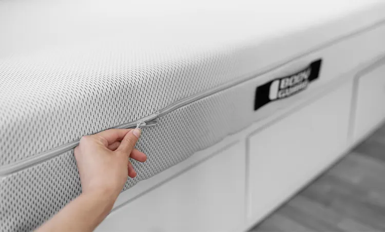 Main ouvrant la fermeture éclair d’un matelas BODYGUARD®, montrant la housse HyBreeze® texturée blanche et grise.