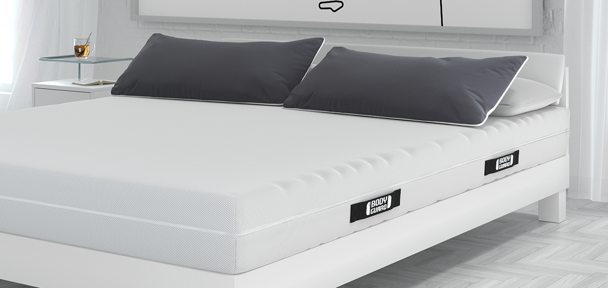 Un matelas BODYGUARD avec deux oreillers habillés d'une taie grise.