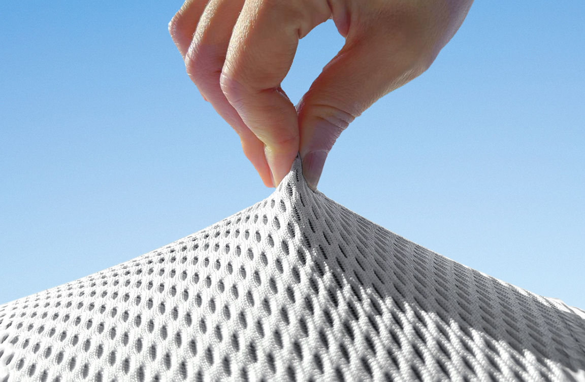Main tirant sur un tissu respirant en maille blanche à motifs alvéolés, sous un ciel bleu.