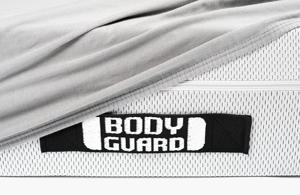 La moitié du matelas BODYGUARD® est recouverte du drap-housse en jersey gris. On voit les poignées noires du Matelas cousues de Bodyguard