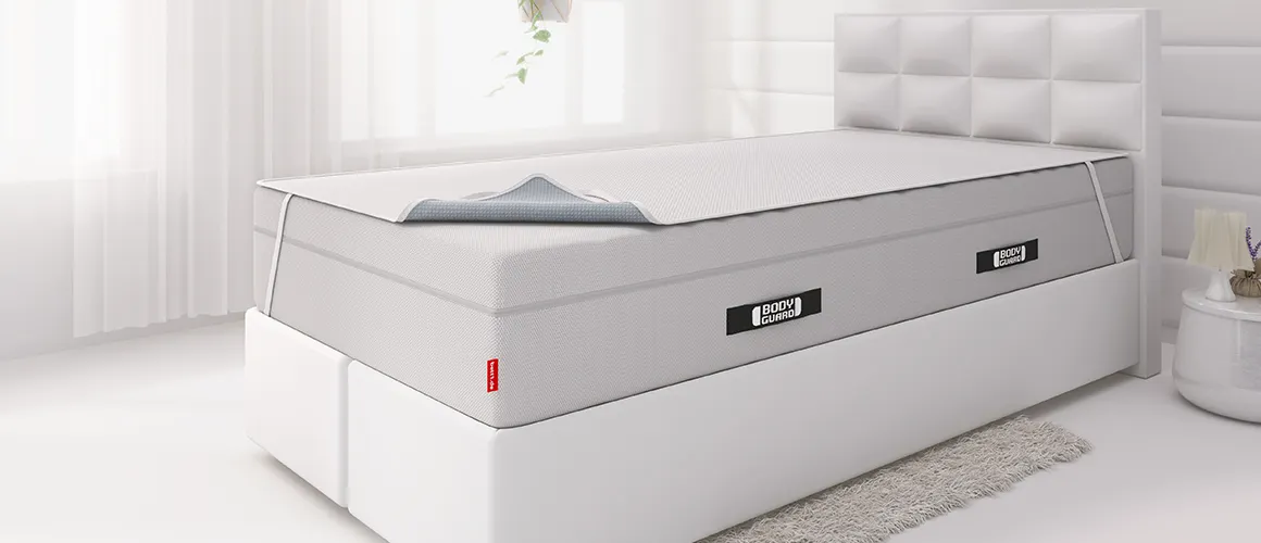 Matelas BODYGUARD® dans une chambre lumineuse, avec surmatelas partiellement replié et étiquette bett1 visible.
