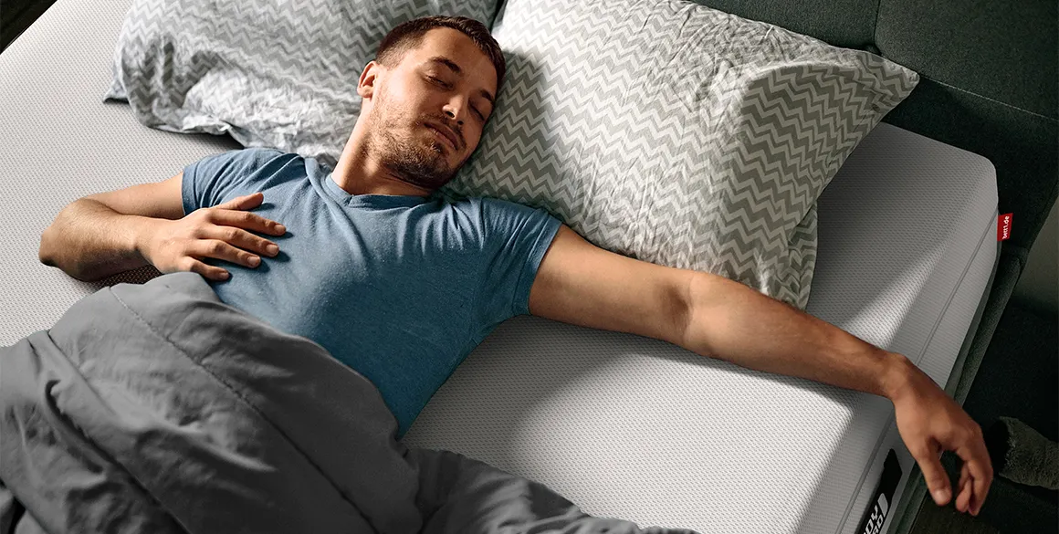 Homme endormi sur un matelas BODYGUARD®, allongé sur le dos et les bras écartés, profitant d’un sommeil paisible.