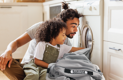 Un père et sa fille regardent à l’intérieur d’un lave-linge, avec une housse BODYGUARD® posée devant.